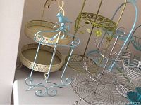 Photo showing blue metal basket stand with bird motif and cream colored round metal baskets