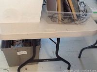 Overall corner view of the table, showing plastic top, metal leg support, and nearby storage bins.