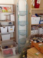 Full view of tall blue metal rack with four circular wire basket shelves against a wall next to shelving units and plastic bins.