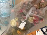 Clear plastic bag containing various faux flowers with different colors and types visible, with stems and petals.