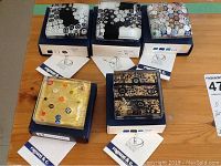 Five Murano glass paperweights on individual boxes with certification cards, showing various floral and geometric millefiori patterns in black, white, yellow, and multicolors.