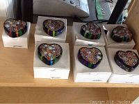Seven Murano heart-shaped glass paperweights on white boxes, displaying colorful millefiori patterns.