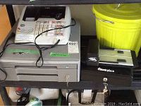 White Casio cash register on top of gray cash drawer, with power cord visible.