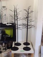 Front view of four black metal jewelry stands with branch designs on a white platform indoors.