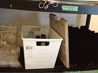 White plastic bin on black metal shelving containing perfume bottles and possibly other items