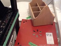 Photo of red metal basket stand with floral cutout pattern and part of wooden basket stand on top.