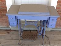 Full view of the painted blue Singer sewing machine cabinet showing the top surface, drawers, and cast iron base with treadle.