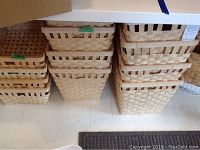 Four stacks of woven baskets arranged on floor under a table, showing different sizes and quantities.