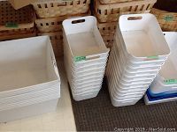 Four stacks of white plastic storage bins. Large bins without handles, medium bins with handles, and smaller bins in varying sizes and shapes.