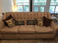 Front view of the large beige sofa with tufted backrest and multiple pillows.