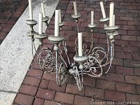 Large rustic metal chandelier with multiple candle-style light holders in aged distressed finish.