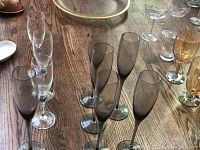 Photo showing six smoke champagne glasses and three additional glasses with clear or amber tint on a wooden surface.