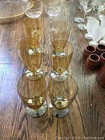 Eight amber-tinted wine glasses arranged on a wooden surface showing full set and color