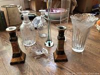Photo showing two vintage glass and metal candle holders, three glass flower vases of different shapes, and two bitters bottles on wooden floor.