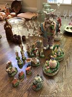 Overview of entire Peter Rabbit collection on wooden table showing large main figurine, small figurines, and glassware background
