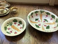 Two hand-painted ceramic bowls with radish and carrot motifs on a wooden surface. One bowl is larger, the other medium-sized.