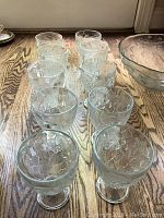 Photo of 10 clear textured water glasses with raised grapevine pattern on a wood floor, showing their shape and design.