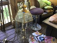 Glass and brass hanging chandelier showing its glass panels and brass framing with attached chain and candle-style bulbs inside, displayed near window.