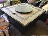 Overview photo of the fire pit table showing the composite top with glass insets, metal edge, and rattan woven base.