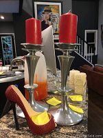 Photo showing two silver metal candle holders with red pillar candles and red shoe wine holder on granite countertop.