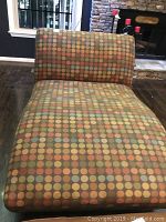 Front view of upholstered chaise lounge showing patterned fabric with multi-colored dots in orange, blue, and yellow on brown background.