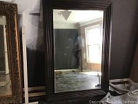 Full view of large rectangular mirror leaning against wall, showing its size and reflective surface.