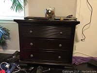 Full front view of dark wooden chest of drawers with three drawers and round metal knobs.