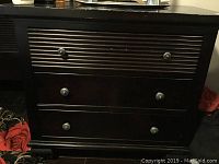 Front view of wooden chest of drawers showing three drawers with metal knobs and ribbed top drawer.