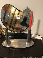 Two metal IKEA candlesticks placed on metal oval tray, one red taper candle inserted in one candlestick.