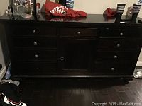 Full frontal view showing 8 drawers and 1 door, dark wood finish, minor wear on top surface.