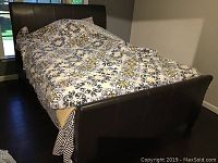 Full view of the brown faux leather bed frame with bedding on it, showing the footboard and partial side.