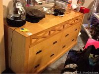Front and side view of light-colored wood dresser with six drawers, black metal handles, and some wear marks and stains on surface.