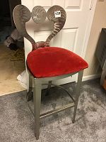 Front view of a metal chair with curved, patterned backrest and red seat cushion.