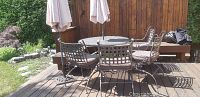 Overview of round metal table with four chairs, two umbrellas on wooden deck