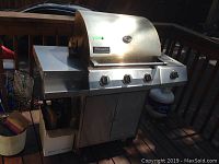 Front view of the three-burner stainless steel grill with closed hood, control knobs and folded side shelf