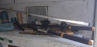 Shelf with various tools and garden hose attachments, including an axe, long level, saw, and green twine.