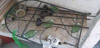 Photo of black metal garden decoration panel with green glass leaf accents and a solar garden light on the ground.