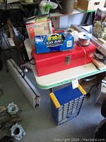 Red metal toolbox, rolls of wire, box of disposable gloves, and other small accessories on top of a white table.