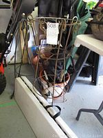 Metal wire plant stand with detailed decorative loops, standing next to folded bench and several flower pots underneath.