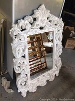 Full view of large rectangular wall mirror with thick white decorative frame containing carved floral and leaf patterns.