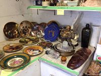 Shelf display with multiple collector plates, Buddha fountain, carved wooden mask, and other decorative items