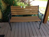 Full front view of the outdoor bench showing wood-look plastic slats and cast iron side supports on a deck.