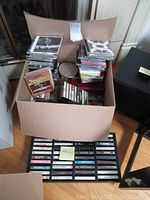 Box filled with multiple stacks of CDs and two trays of cassette tapes