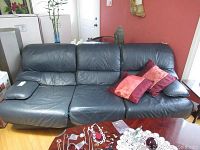 Front view of midnight blue three-seater leather couch with red throw pillows on right armrest and cushions.