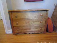 Front view of antique wooden dresser with three drawers and decorative inlay on middle drawer.
