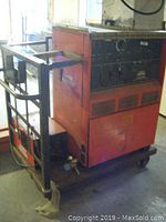 Overall view of red welder on wheeled platform with side guard rail