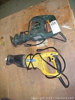 Two reciprocating saws on wooden surface, green Bosch and yellow Power Fist, with power cords visible.