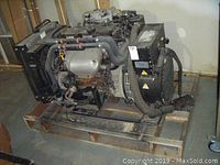 Full side view of the generator engine mounted on a wooden pallet showing hoses, radiator, and mounting frame.