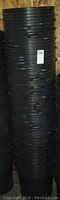 Tall stack of black plastic plant buckets with a label on the side.