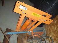 Top angle view of orange hydraulic pipe bender showing the metal frame, hydraulic jack, and adjustable holes.